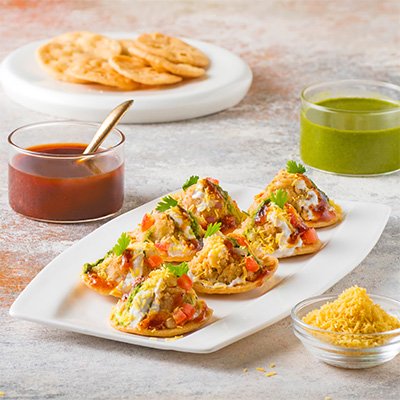 A colorful serving of Sev Puri, featuring crispy puris topped with a mixture of diced potatoes, onions, and tomatoes, drizzled with tangy chutney and garnished with crispy sev and fresh cilantro.