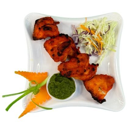 A vibrant plate of Chicken Tikka, featuring tender, marinated chicken pieces grilled to perfection, garnished with fresh cilantro and served with a side of tangy mint chutney.